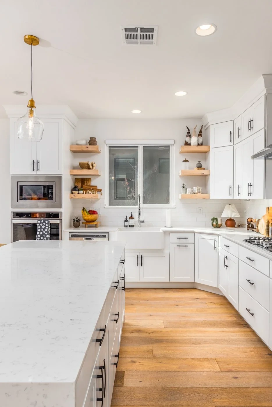 Modern white kitchen with wooden floors, open shelving, and a central island with white marble countertop.
