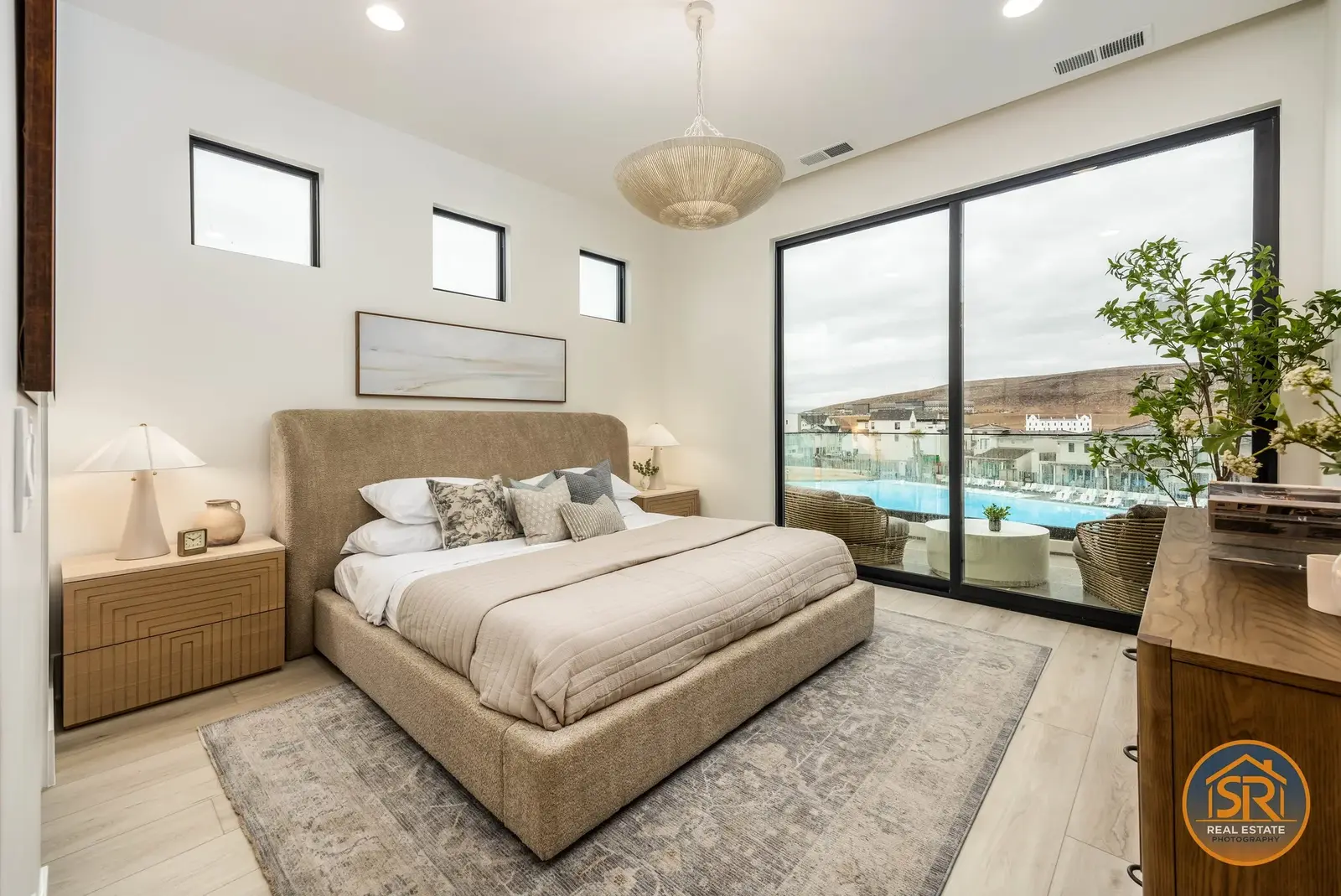 Bedroom with a neutral upholstered bed and large windows overlooking the pool.