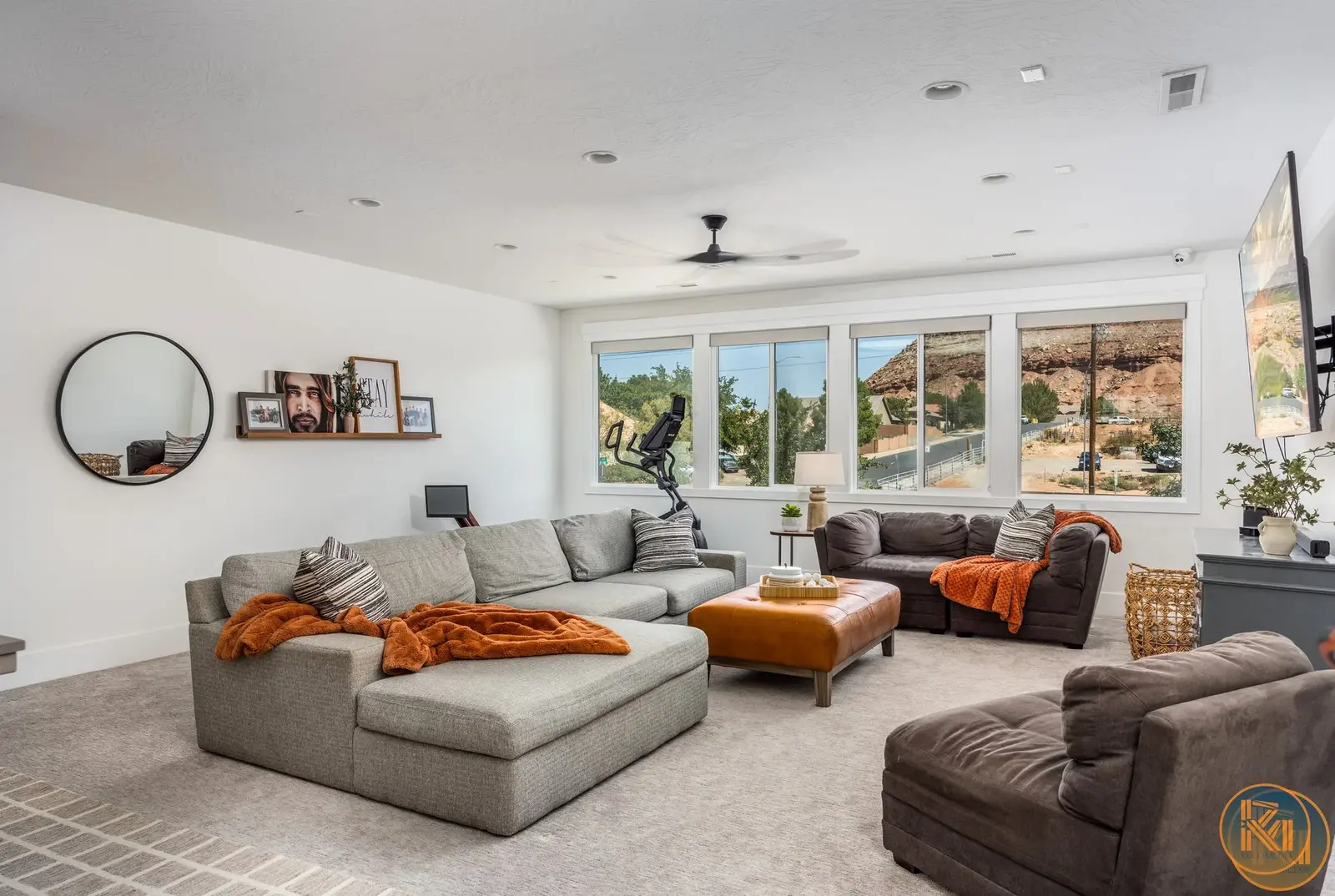 Open living room with a gray sectional, orange accents, and large windows.