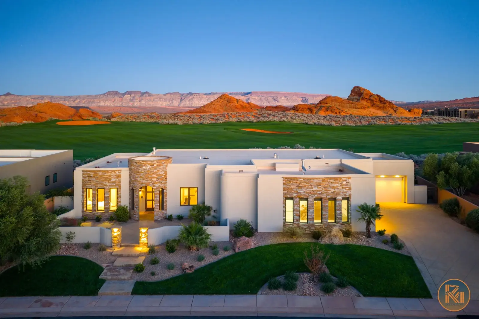 Illuminated home beside a golf course with red-rock scenery at dusk.